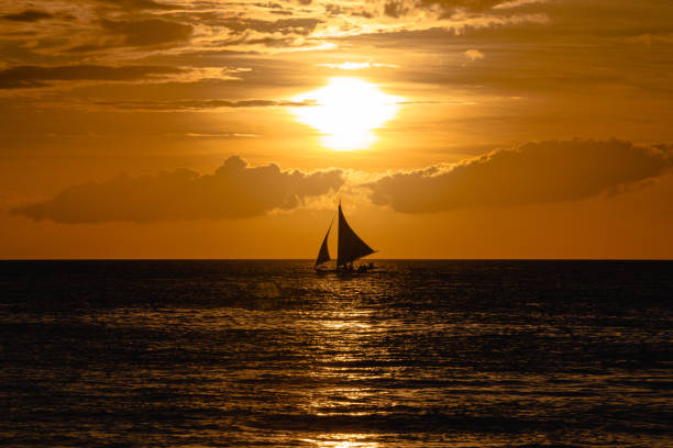 istock One outrigger sailboat on the horizon at sunset 953695640