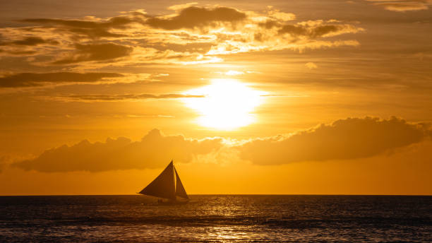 istock One outrigger sailboat on the horizon at sunset 953695676