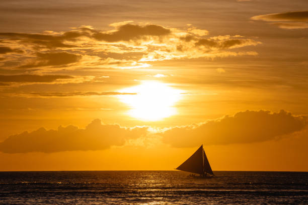 istock One outrigger sailboat on the horizon at sunset 953695900