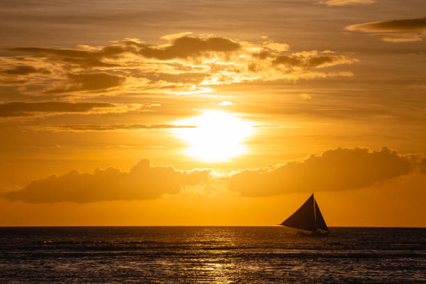 istock One outrigger sailboat on the horizon at sunset 953695960