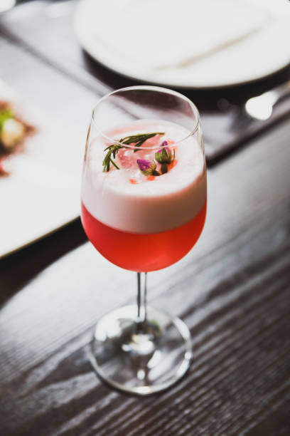 Red cocktail in wine glass topping with foam, flowers and rosemary.