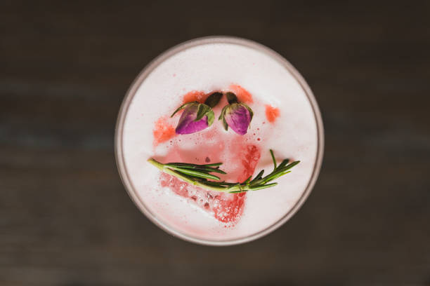 Red cocktail in wine glass topping with foam, flowers and rosemary.