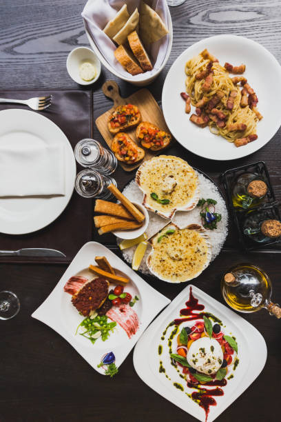 istock Italian dishes on the table including Burrata Salad, Baked Cod with sauce,  Spaghetti Carbonara, Baked scallops with cheese and Canapes with olive oil, pepper and salt on the table. 953705006