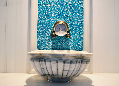 A classic Turkish bath sink with light blue textured marble background.
