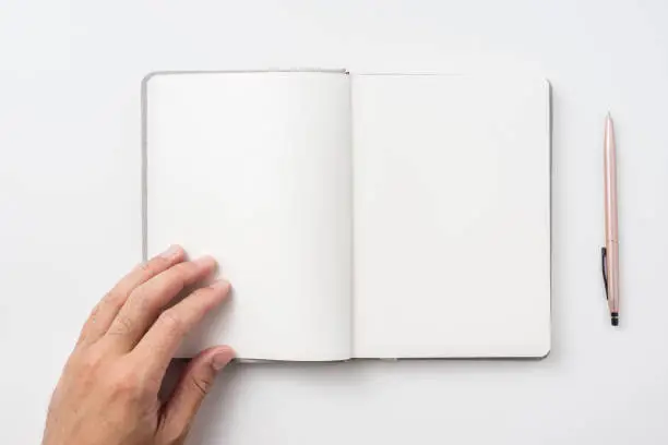 Photo of Top view of man's hand holding hardcover gray linen notebook  and ballpoint pen