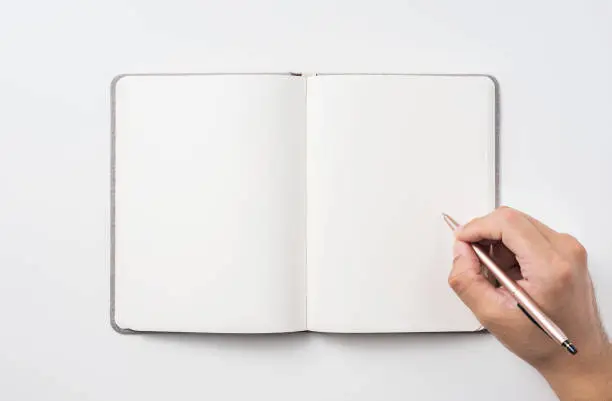 Photo of Top view of man's hand holding hardcover gray linen notebook and ballpoint pen