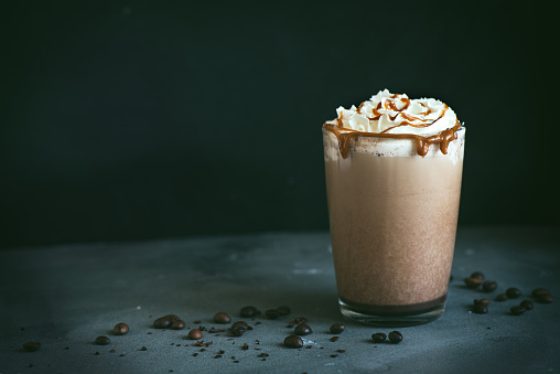 Cold Frappe Coffee (frappuccino) with whipped cream and caramel on dark background, copy space.