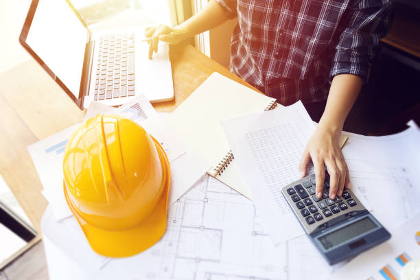 ingeniero asiático, arquitecto mujer usando la calculadora para la contabilidad y análisis de estructura de edificio de plano y papel carta delante de ordenador portátil en el espacio de trabajo de oficina. - construction document clothing architect fotografías e imágenes de stock