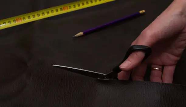 Woman hand cutting brown leather using scissors, pencil and yellow tape measure