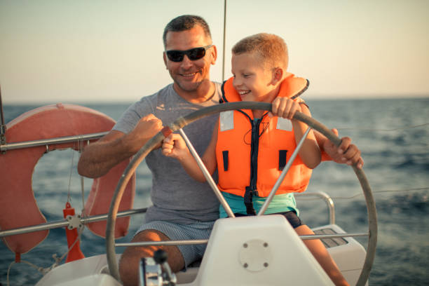 istock Little boy sitting with father and steering with sailboat 953774530