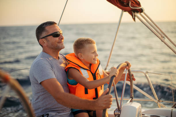 istock Little boy sitting with father and steering with sailboat 953774532
