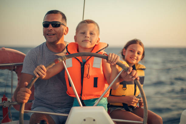 istock Little boy sitting with father and steering with sailboat 953774770