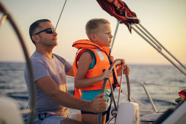 istock Little boy sitting with father and steering with sailboat 953774772
