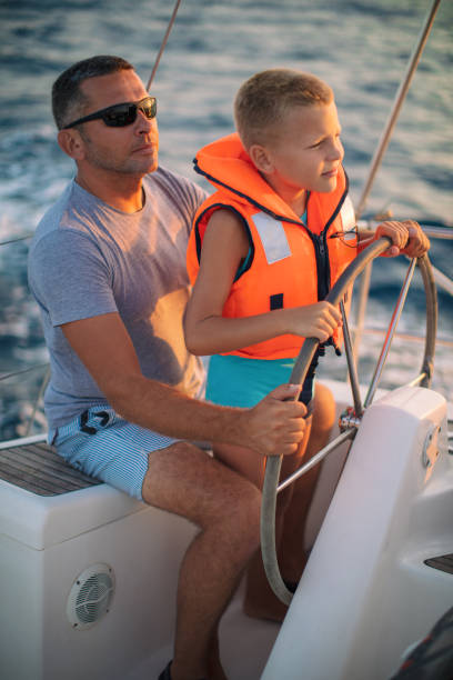 istock Little boy sitting with father and steering with sailboat 953774892