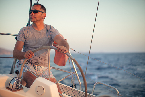 One man on sailboat enjoying at summer and having a fun while steering with yacht at sunset