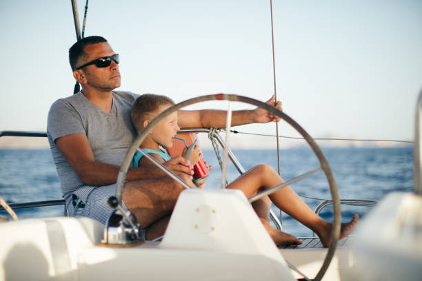 istock Little boy sitting with father who steering with sailboat 953779144