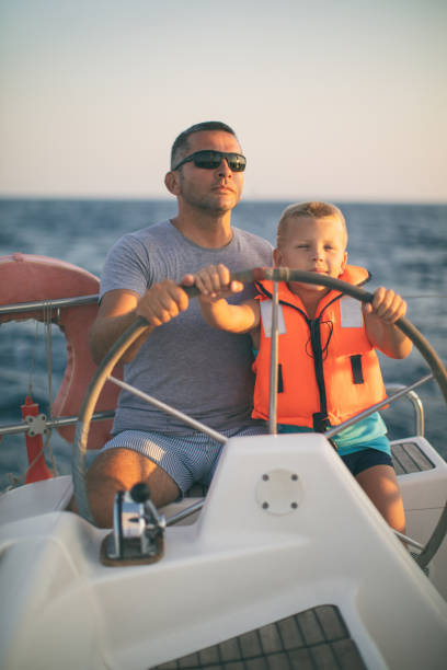 istock Little boy sitting with father and steering with sailboat 953779482