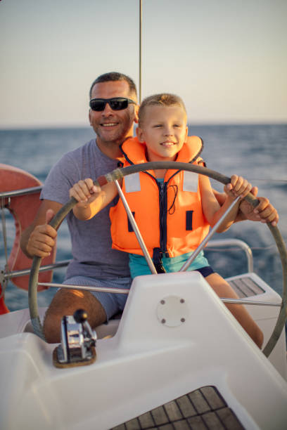 istock Little boy sitting with father and steering with sailboat 953779564