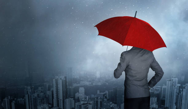 businessman standing while holding an red umbrella over storm in city huge rain background. business crisis and insurance concept. - protection insurance dark rain imagens e fotografias de stock