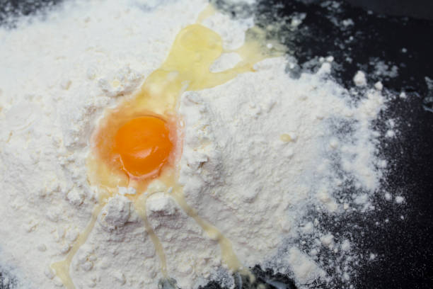 istock Chicken eggs in white plate and slide around her meal with a broken egg. The process of making of the test. Eggs, flour, a plate on a black background. 953783700