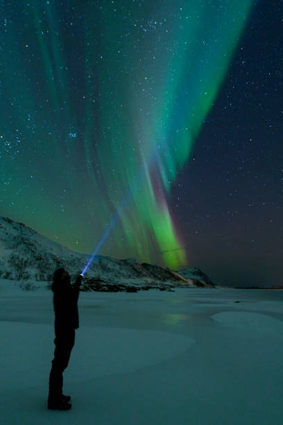 istock Man with a flashlight looking at Northern Lights, Aurora Borealis over the Lofoten 953786866