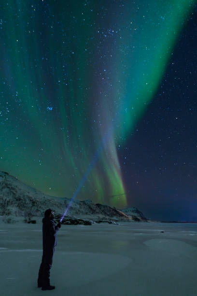 istock Man with a flashlight looking at Northern Lights, Aurora Borealis over the Lofoten 953787614