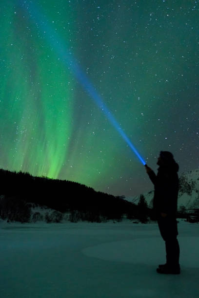 istock Man with a flashlight looking at Northern Lights, Aurora Borealis over the Lofoten 953787930