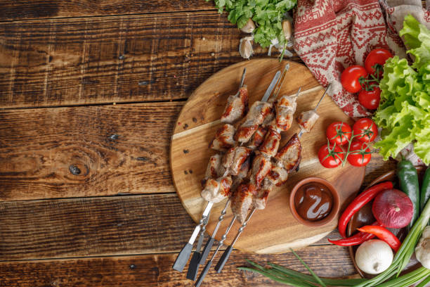 istock Shish kebabs laid out on a wooden board. Appetizing meat cooked on an open fire. Still life with meat and fresh vegetables. 953787988