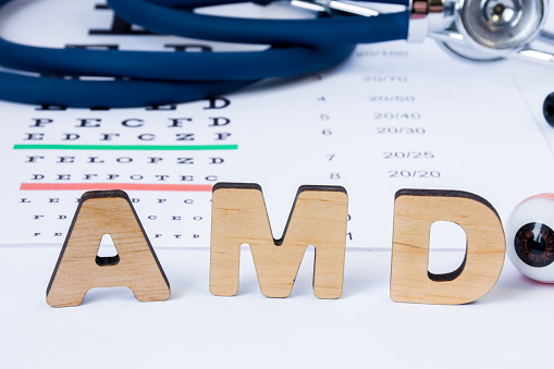 AMD Abbreviation or acronym of age-related macular degeneration - eye problem in older persons. Word AMD is on foreground near eye model with stethoscope and visual acuity test on blurry background