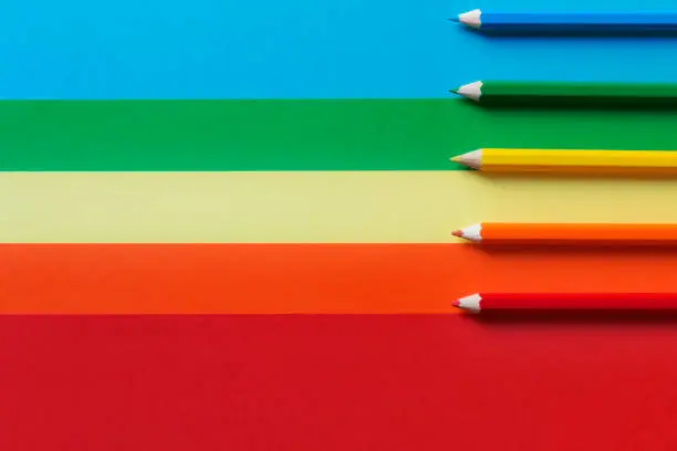five different colored pencils on a multicolored background.A horizontal and graphic composition, rainbow effect