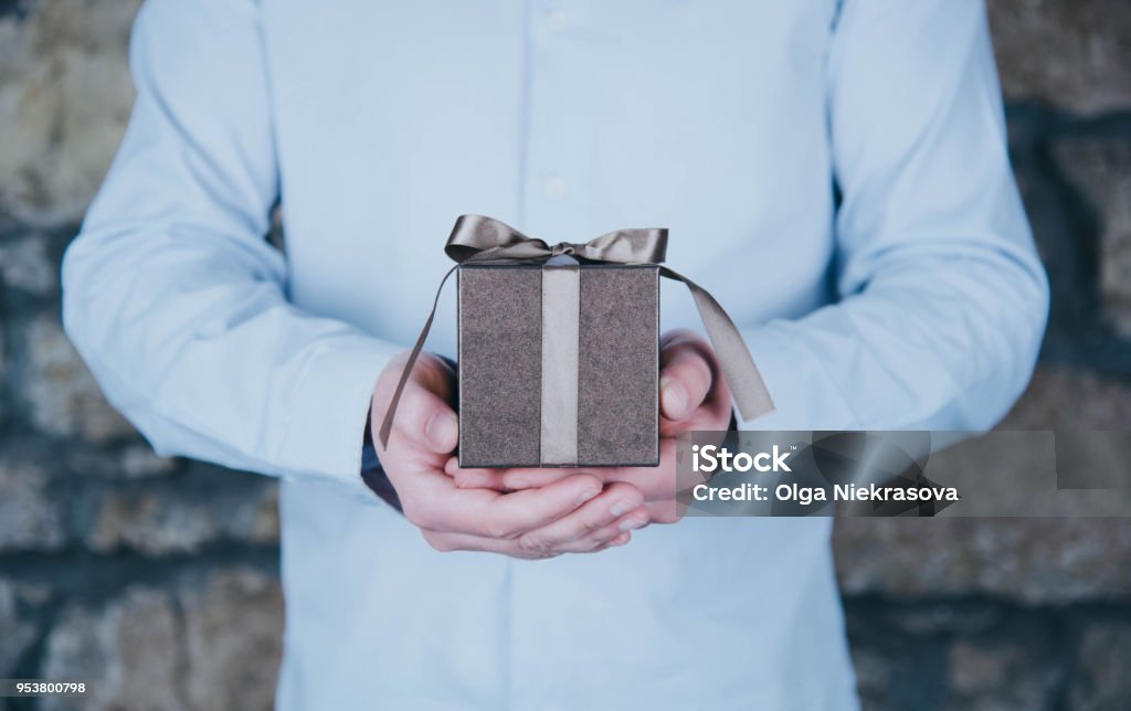 Male hands holding a gift Male hands holding a gift against rustic background. Gift Stock Photo