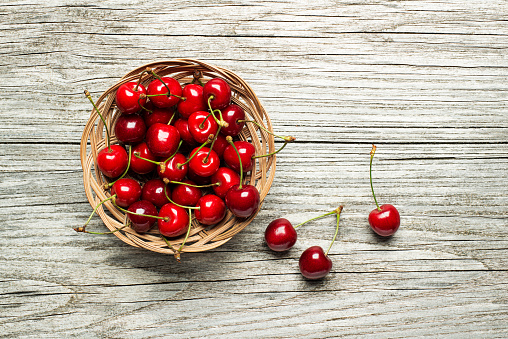 Fresh red cherries in basket on wooden table