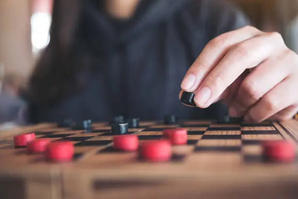 Photo of Closeup image of people playing and moving checkers in a chessboard