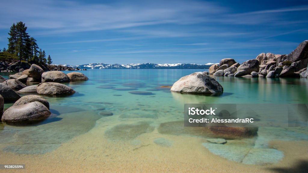 Sand Harbor Lake Tahoe Long exposure blue sky Long exposure of Sand Harbor at Lake Tahoe North, Nevada county, California, USA, featuring blue transparent water, rocky shore and snow on tops of background mountains on a blue sky day with few clouds- travel California North Stock Photo