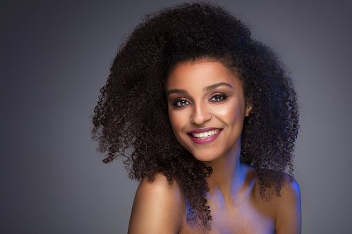 Beauty portrait of smiling dark skin young woman with curly afro hair and glamour makeup. Studio  shot on gray background, copy space.