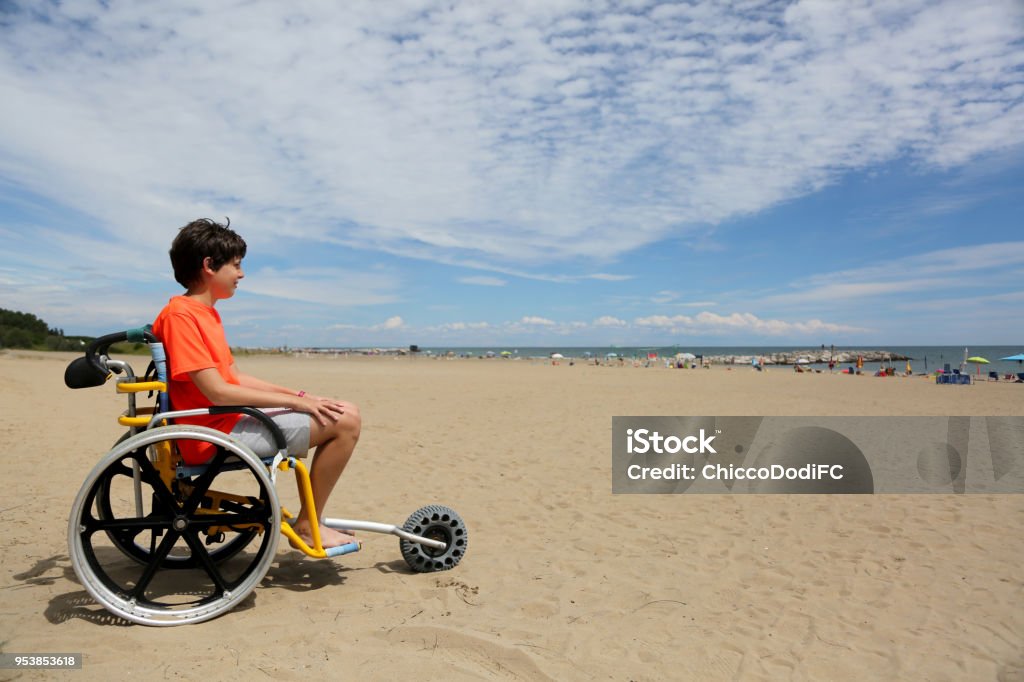 Junge mit orange T-shirt sitzt auf den speziellen Rollstuhl mit einer - Lizenzfrei Rollstuhl Stock-Foto