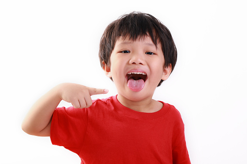 Photo of a little Asian boy pointing at he tongue, isolated on white background.