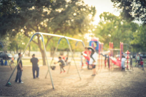 Blurred motion kids swing back and forth at public playground in USA Vintage blurred kids on swing at busy public playground in USA. Defocused children, parents doing activity together. Hanging seat suspended from bar back, forth. Colorful playground in background playground stock pictures, royalty-free photos & images