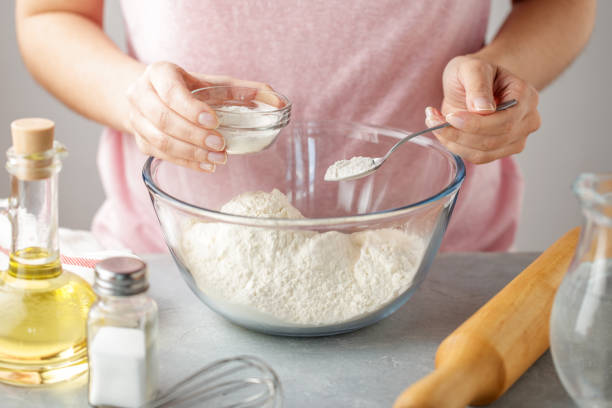 Women adds the baking powder into the glass bowl with flour. stock photo