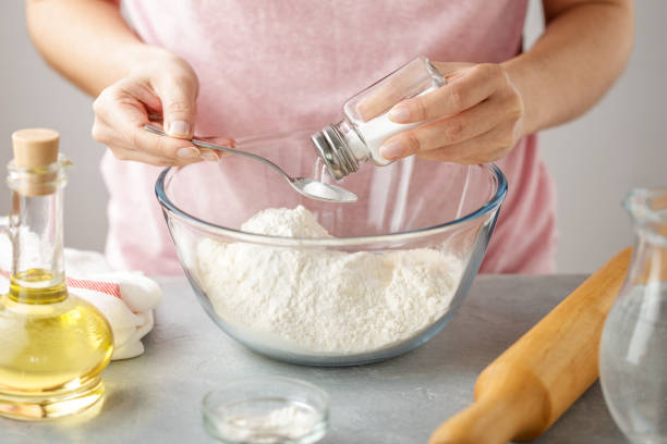 Female hands add salt into glass bowl with flour. stock photo