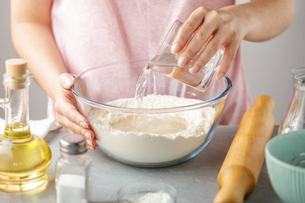 Woman pour hot water into bowl with flour, baking powder, salt and oil. stock photo
