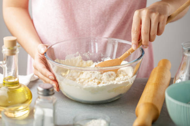 Woman mix flour, baking powder, salt, oil and hot water in the glass bowl. stock photo
