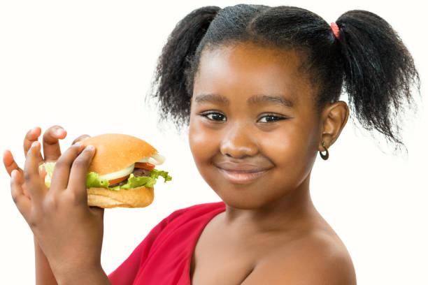 Cute little african girl holding appetizing hamburger. Close up portrait of cute ponytailed african girl holding appetizing hamburger.Kid smiling at camera isolated on white background. spanish hamburger stock pictures, royalty-free photos & images