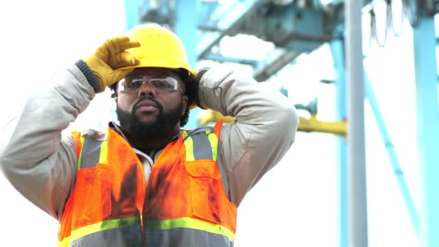 Worker at shipping port near crane, puts on hardhat
