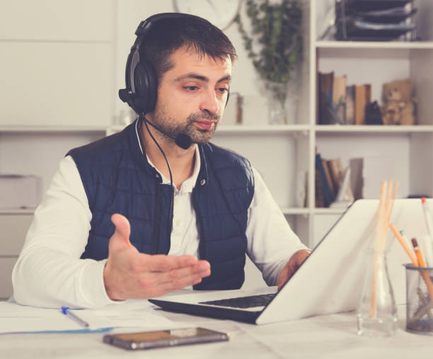 istock Young male employee with headset and laptop at table 953905468