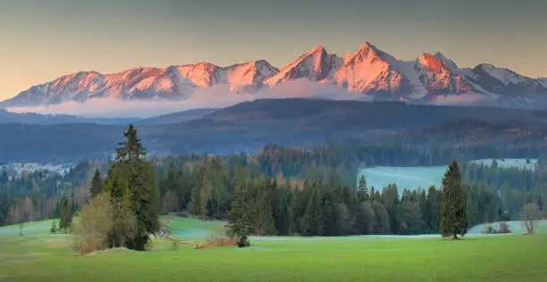 Panoramic view of Tatra mounains.Tatra mountains in the morning. Beautiful green valley at snowy mountains foothills. Picturesgue morning landscape.