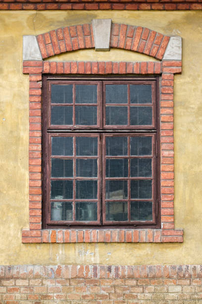 istock Old window on yellow building facade, with decorative brick frame and arch 953916160