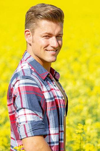 portrait of handsome blond man with open shirt standing in a yellow field