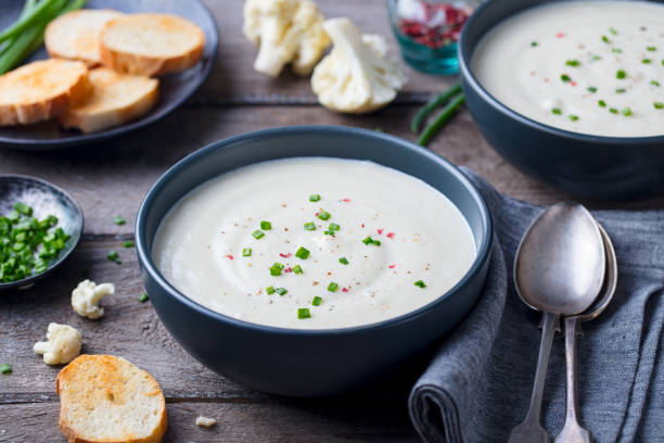 Cauliflower and potato cream soup with green onion in a bowl on grey wooden background.