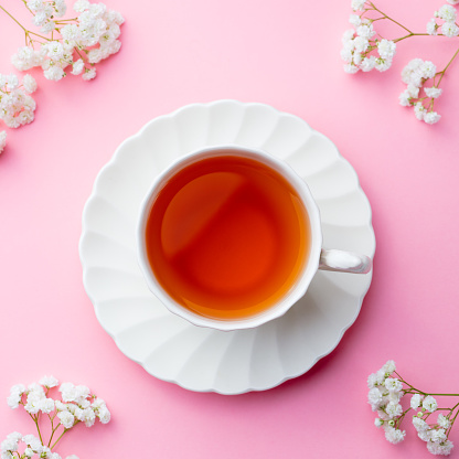 Cup of tea with fresh flowers on pink background. Top view. Copy space.
